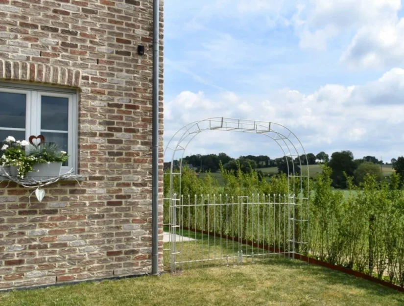De doorgang tussen het huis en de heg wordt afgesloten met een rozenboog met poort.