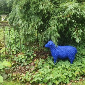 Ein blaues Schaf unter dem Bambus vor dem Eisenzaun