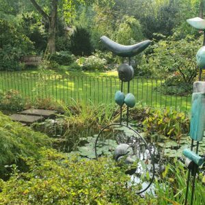 Dekorative Gartenfiguren vor einem Gartenteich mit Zaun aus Eisen