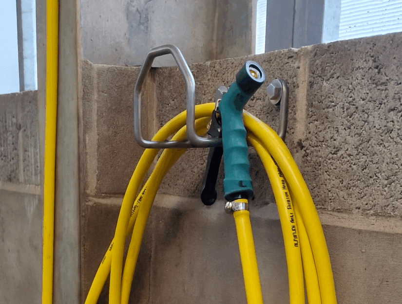 An die Wand geschraubter Schlauchhalter aus Edelstahl in einem landwirtschaftlichen Betrieb.