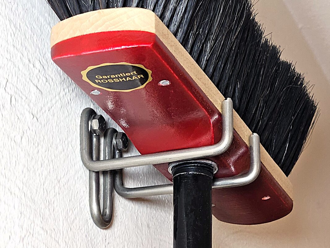 Der Mini-Besenhalter aus Edelstahl, in dem ein Hausbesen hängt.