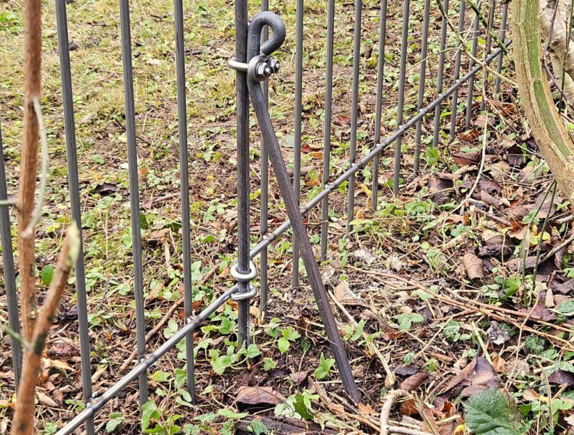Die Abstützstrebe wird im Abstand von 20 cm zum Zaun in den Boden eingeschlagen.
