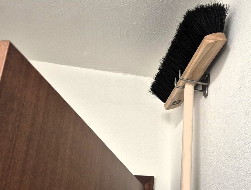 De bezem kan ruimtebesparend achter de deur aan de houder worden opgehangen.