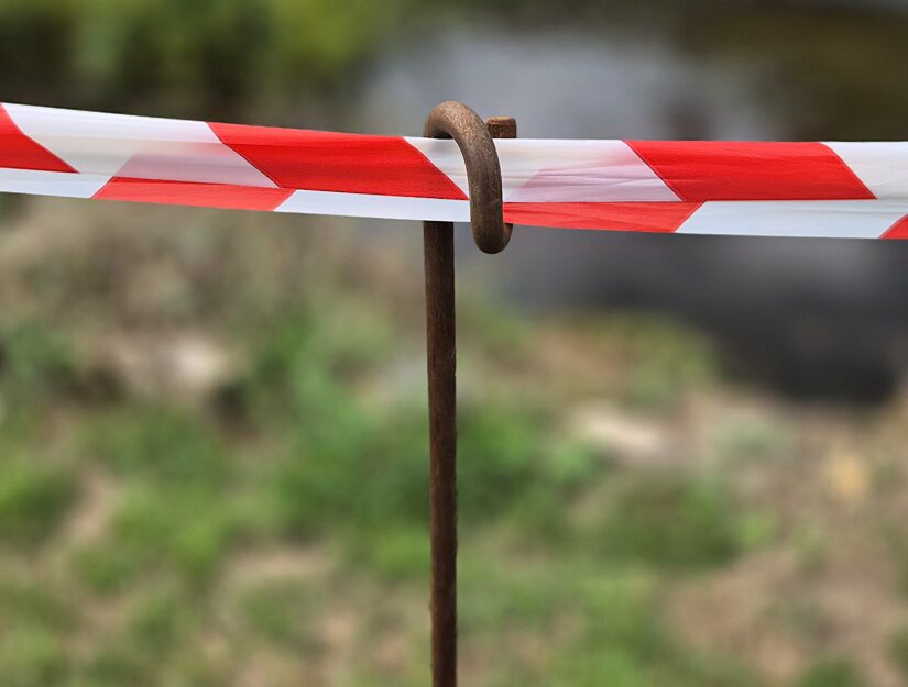 Angerosteter Absperrpfosten mit rot-weißem Absperrband.