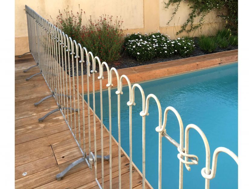 La clôture de la piscine avec porte sur une terrasse en bois.