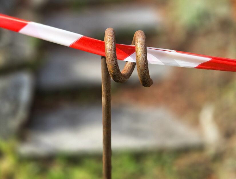 Gestreepte palen met edelroest en een rood-witte afsluitband die eraan is bevestigd.