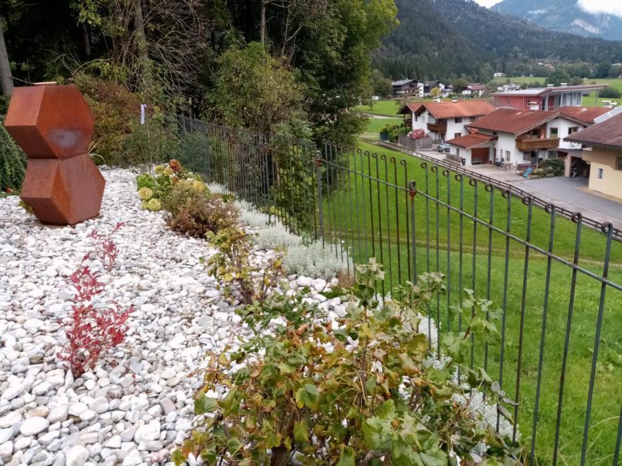 Der Zaun steht am Hang vor der Wiese hinter den weißen Kieselsteinen.