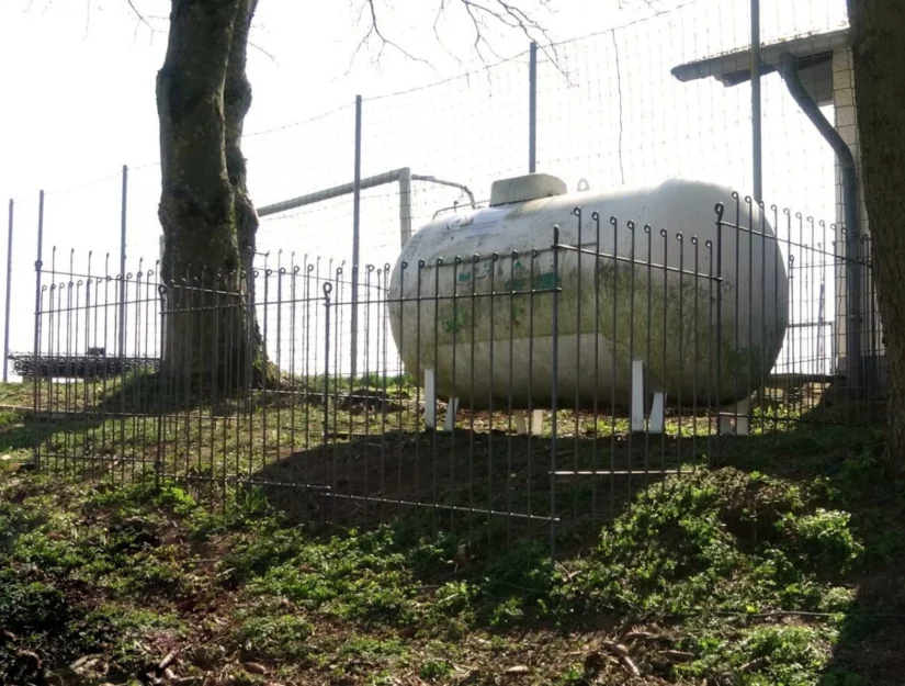 Hekwerk rond een gastank naast een voetbalveld.