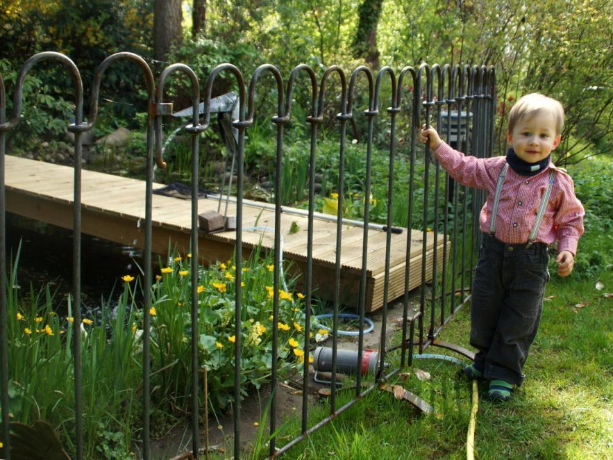 Der Junge hält sich am Zaun fest der verhindert, dass das Kind ins Wasser fällt